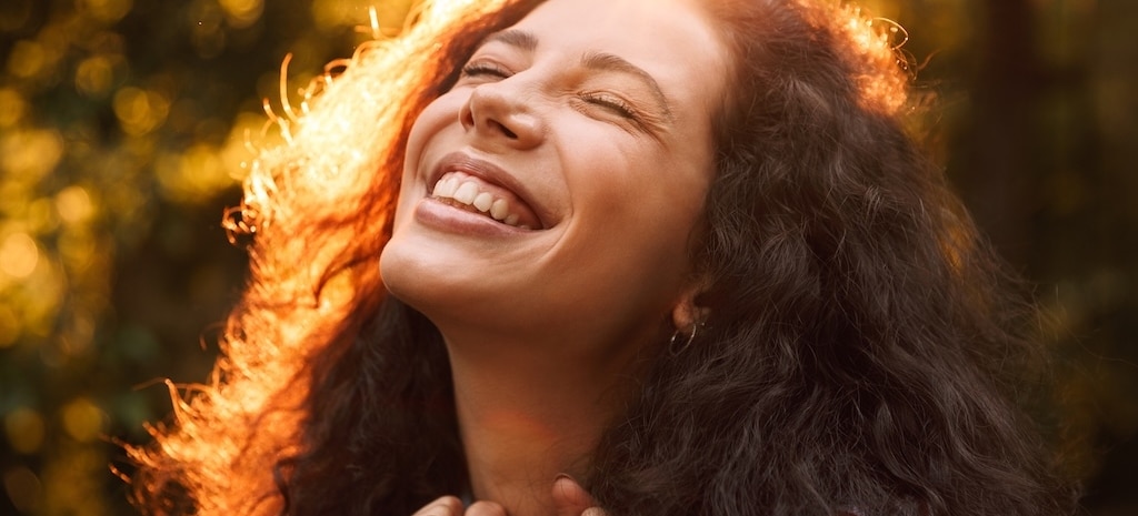 Young woman smiling, looking up at the sun.