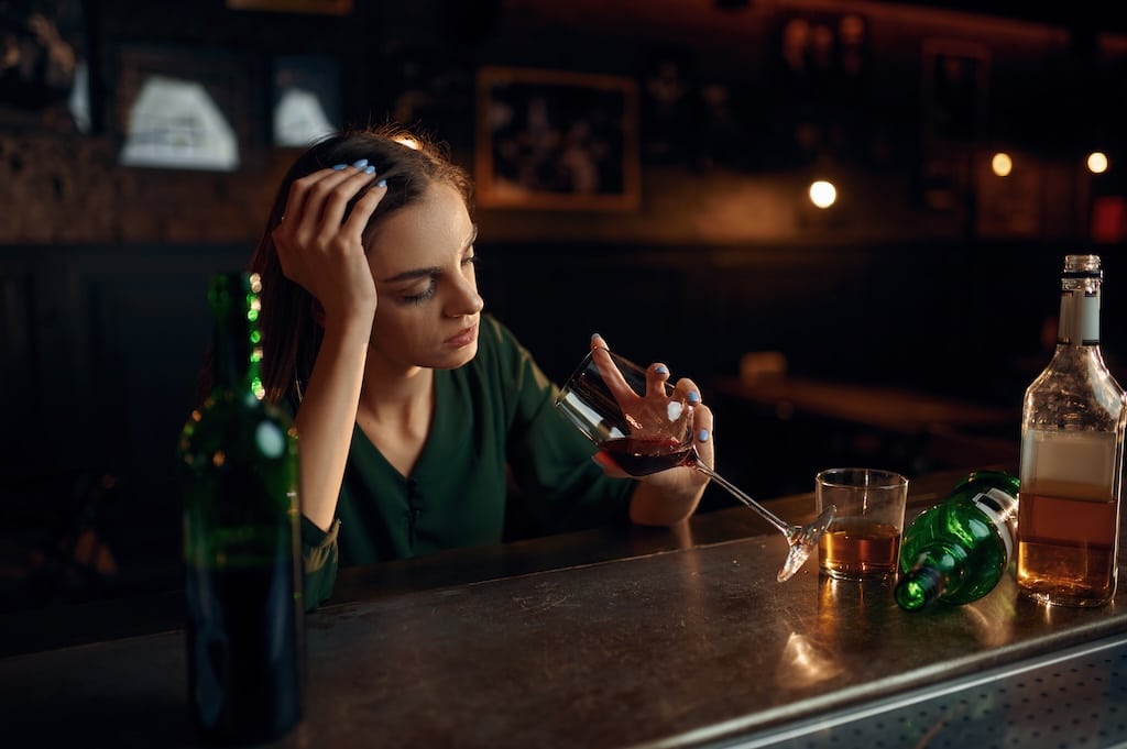 Unhappy woman drinks alcohol beverage at the counter in bar.
