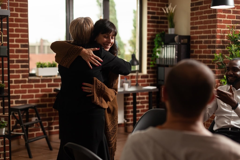 Woman and therapist hugging after sharing recovery progress with group.