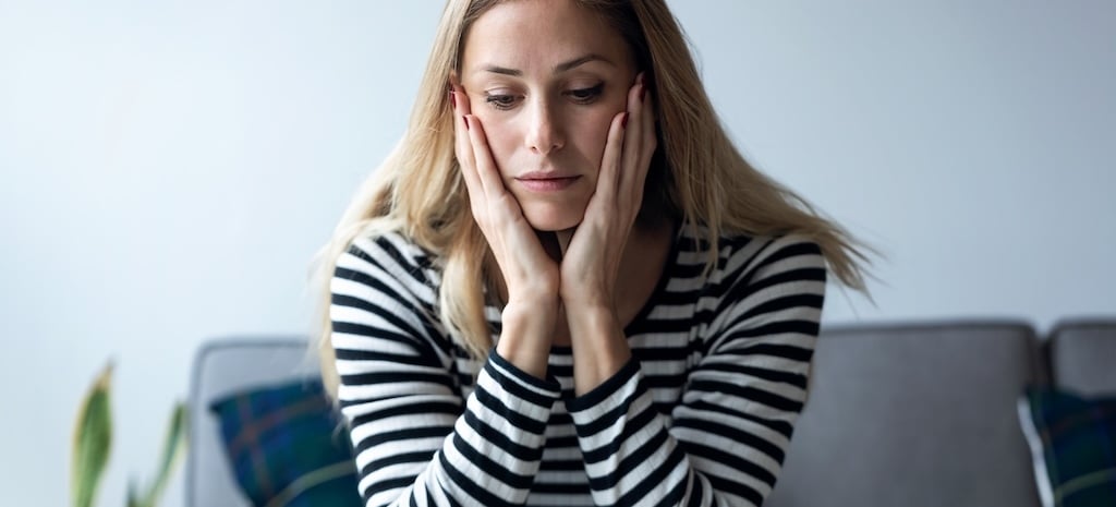 Shot of depressed young woman thinking about her problems while sitting on the sofa at home.