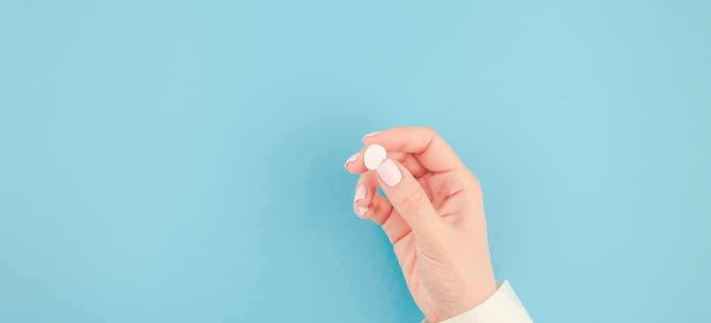 Woman hand holding a white pill on pastel blue paper background