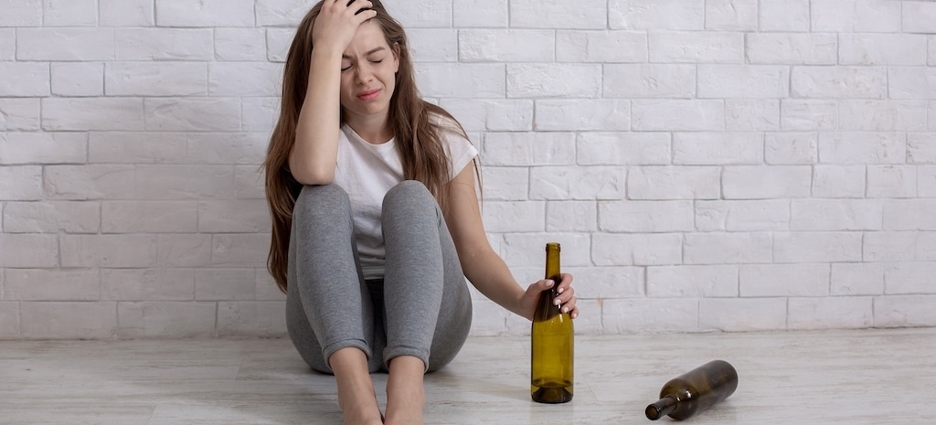 young depressed woman with bottle of booze sitting on floor at home