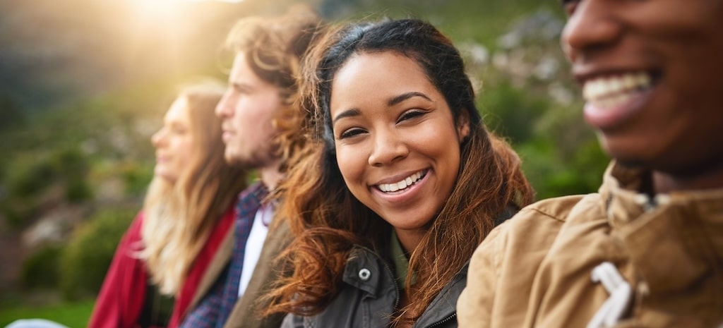Happy young woman smiling, looking at camera while sitting with friends.