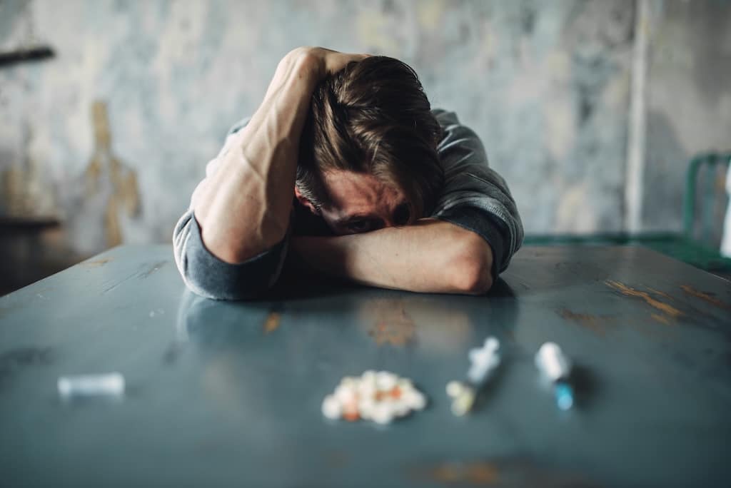 Male sitting at the table with drugs and syringe