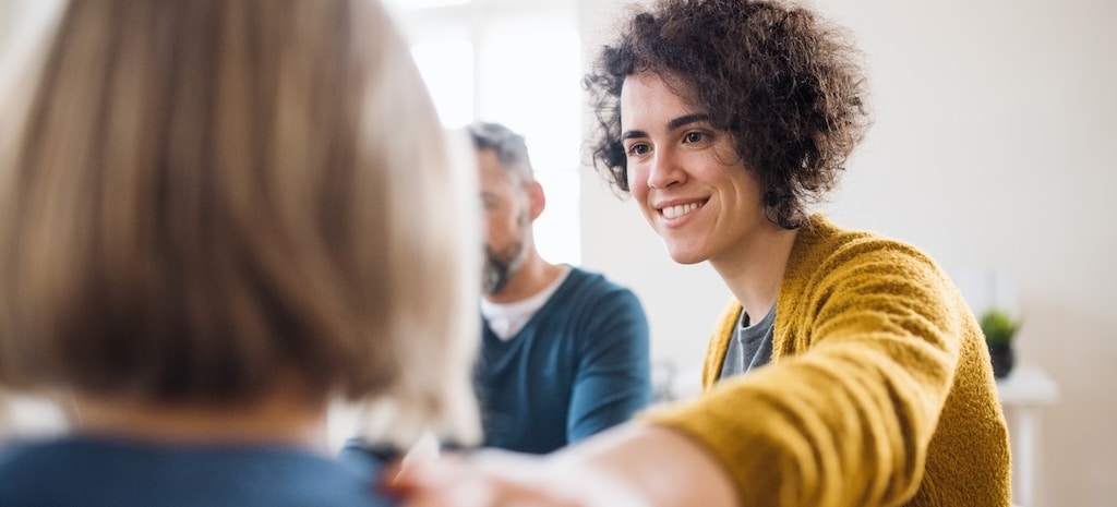 Serious men and women sitting in a circle during group therapy, supporting each other.