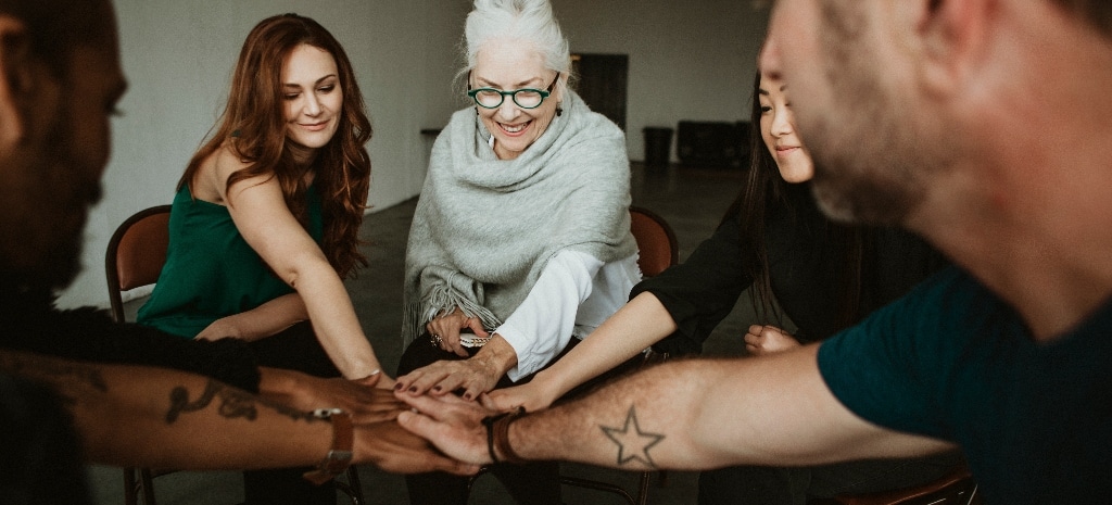 Group of people in recovery putting hands in circle
