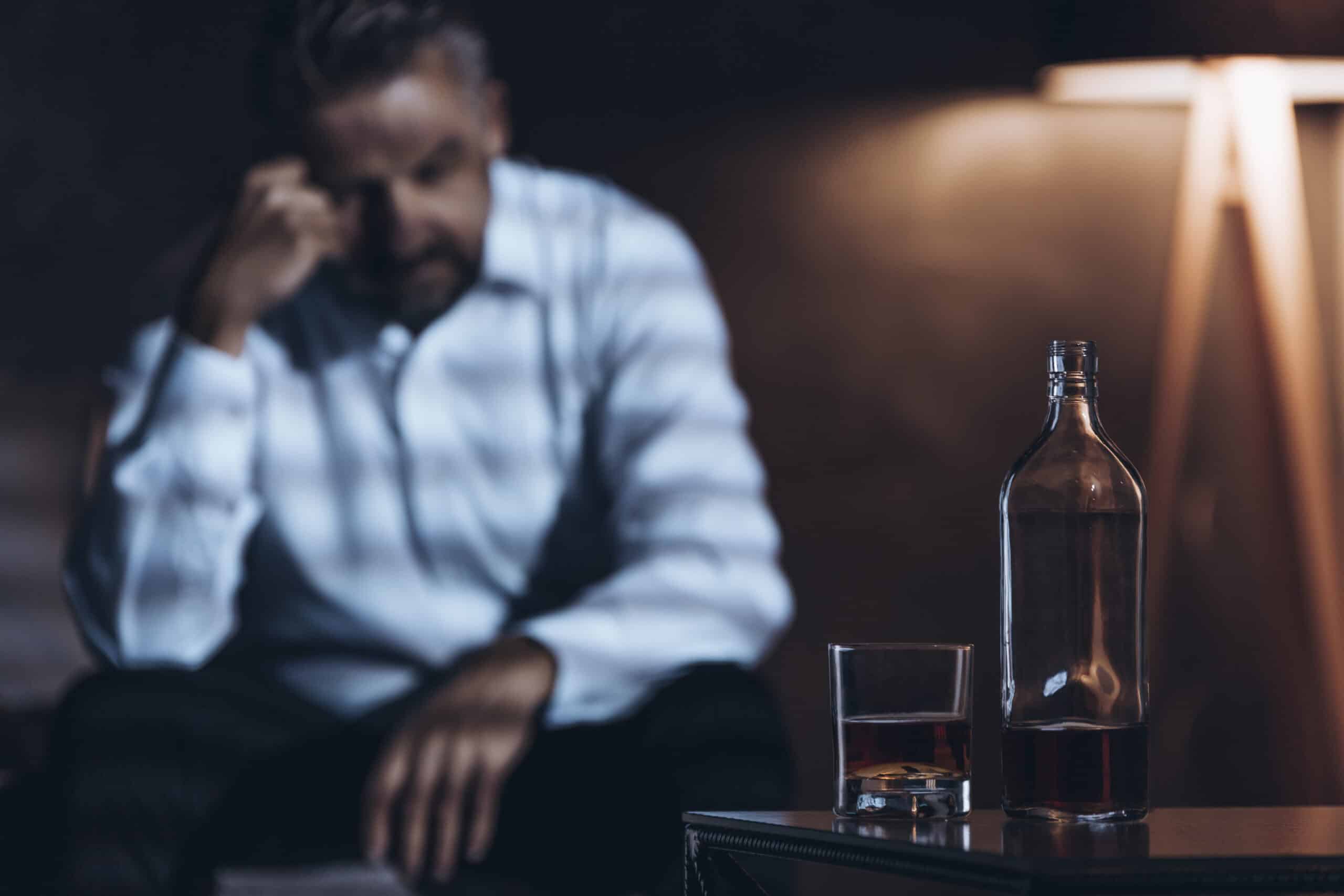 A man with his head down in front of a bottle of alcohol wondering how to taper off alcohol.