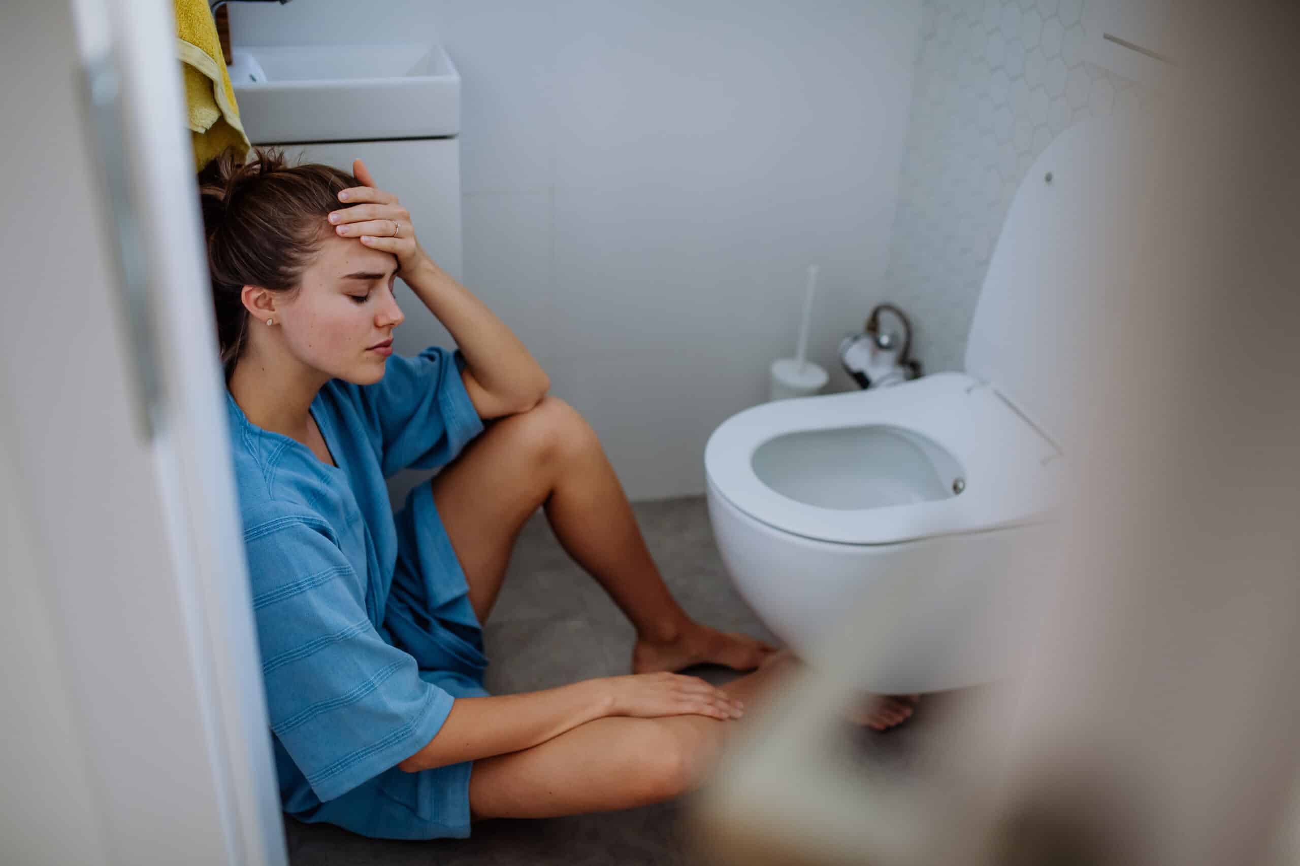 A woman sitting on the floor in front of a toilet worried about vomiting blood after drinking alcohol.