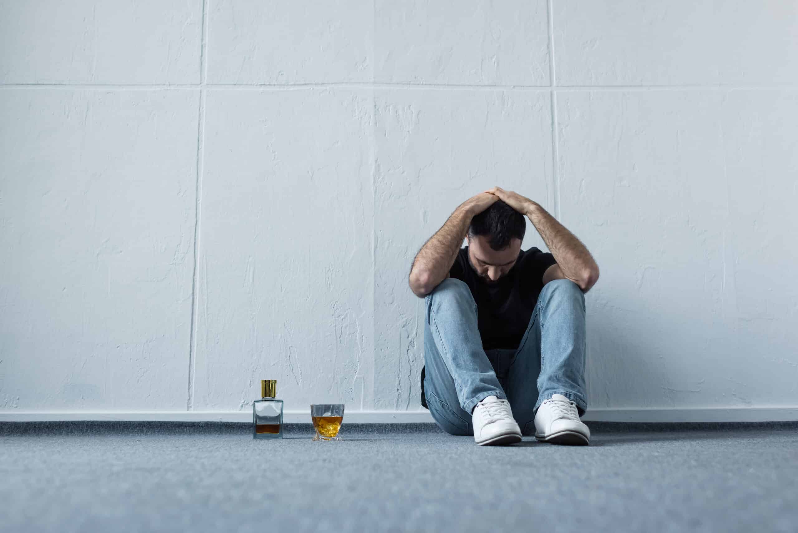 A man sitting with his head down near alcohol for the topic why does alcohol dehydrate you.