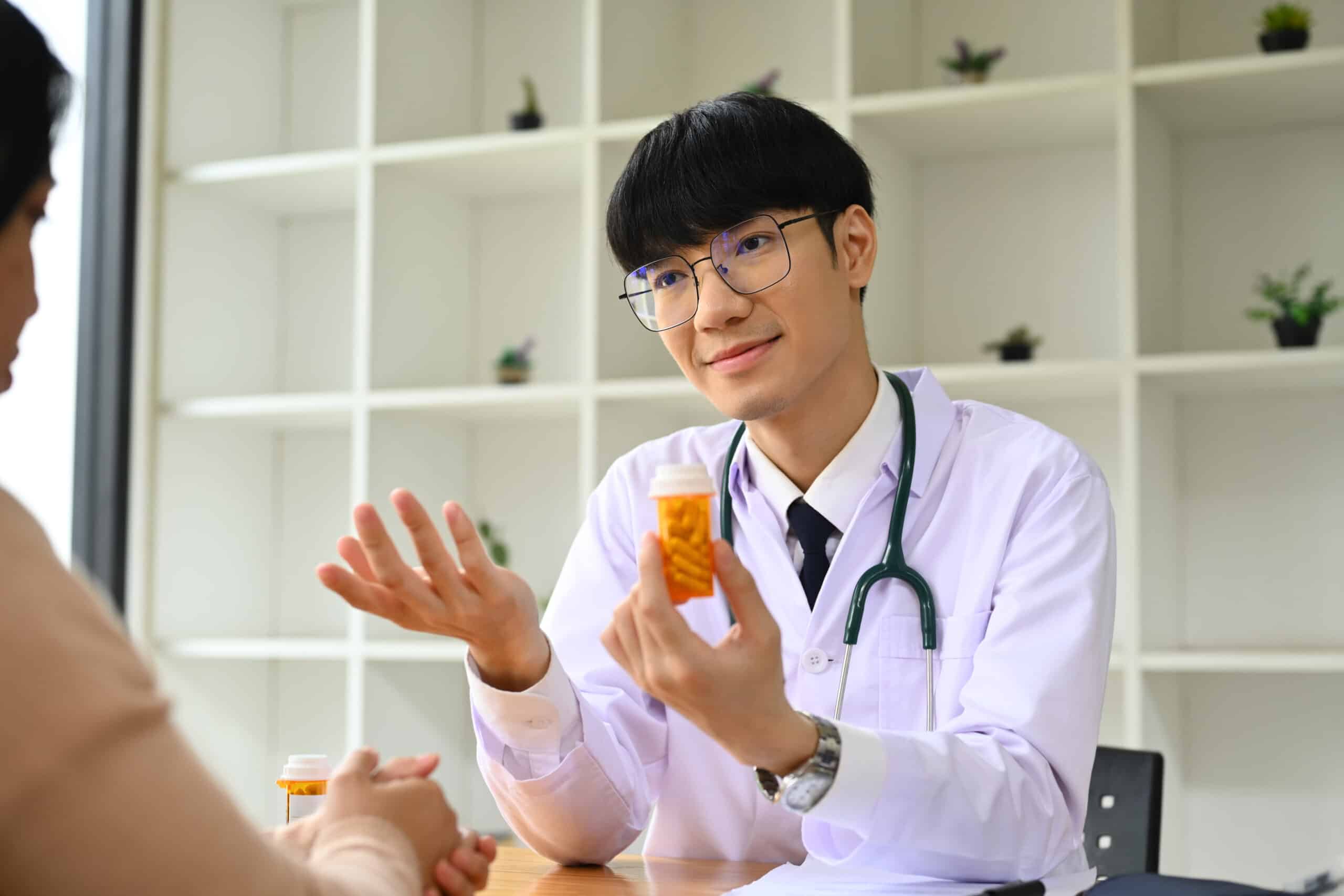A doctor holding up a pill bottle while explaining to a patient the long-term side effects of low-dose naltrexone.