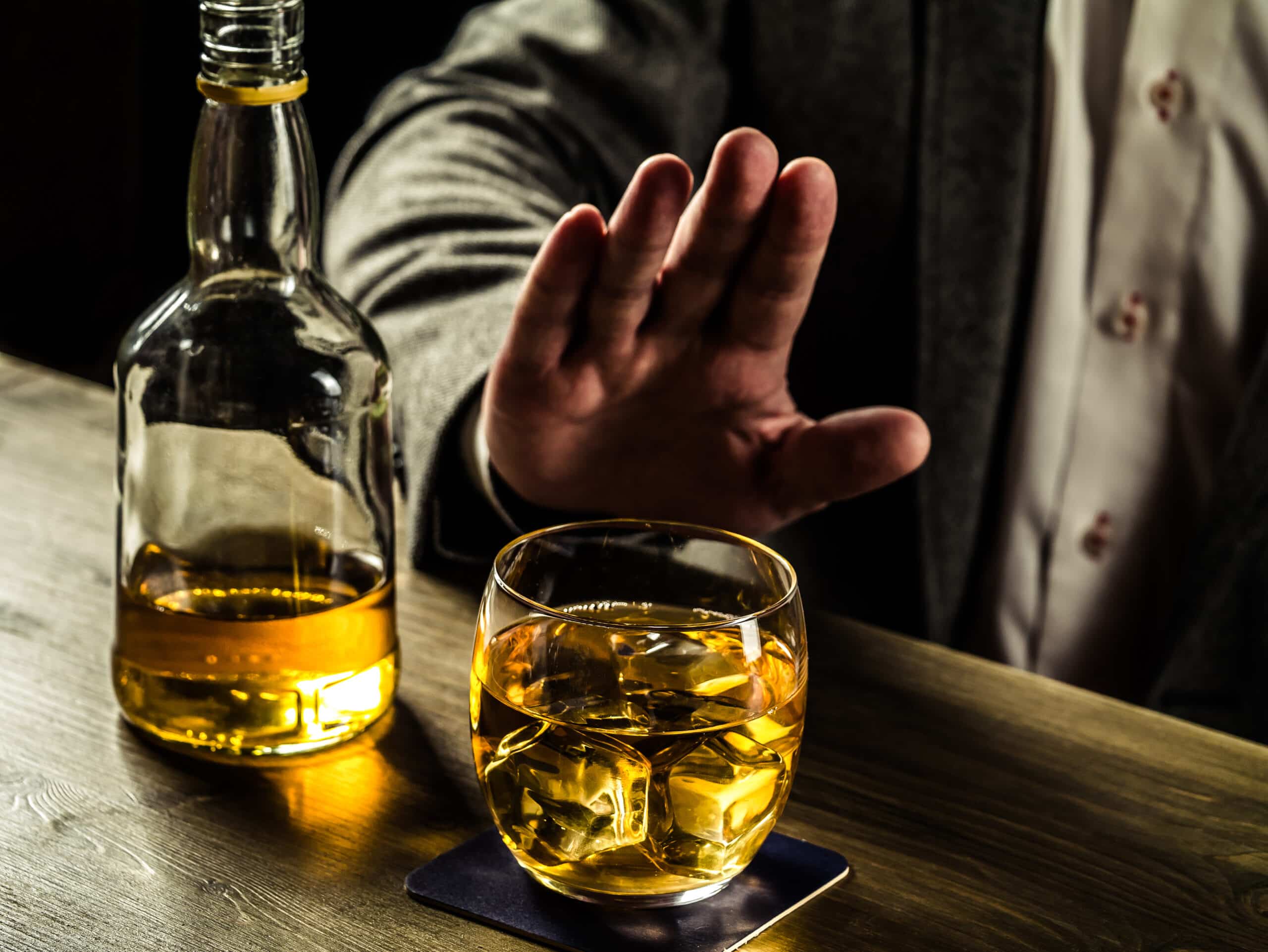 A man putting his hand out to reject a glass of alcohol for the topic quitting drinking timeline.
