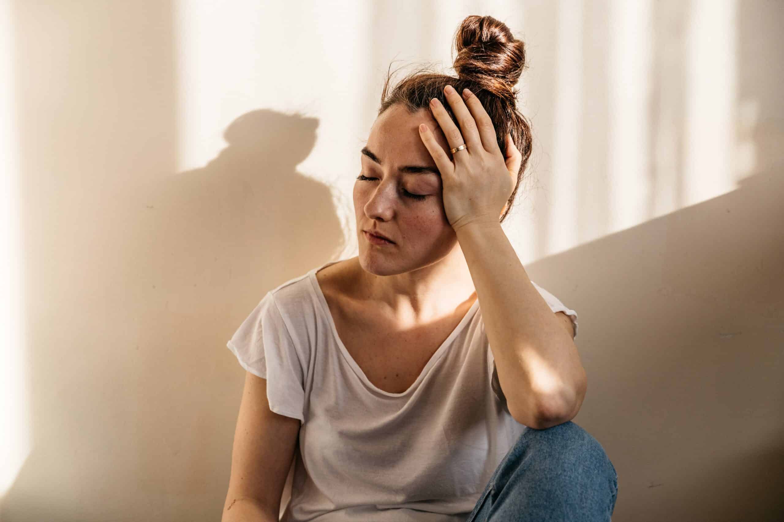 A woman sitting on the floor holding her head while suffering from buspar withdrawal symptoms.