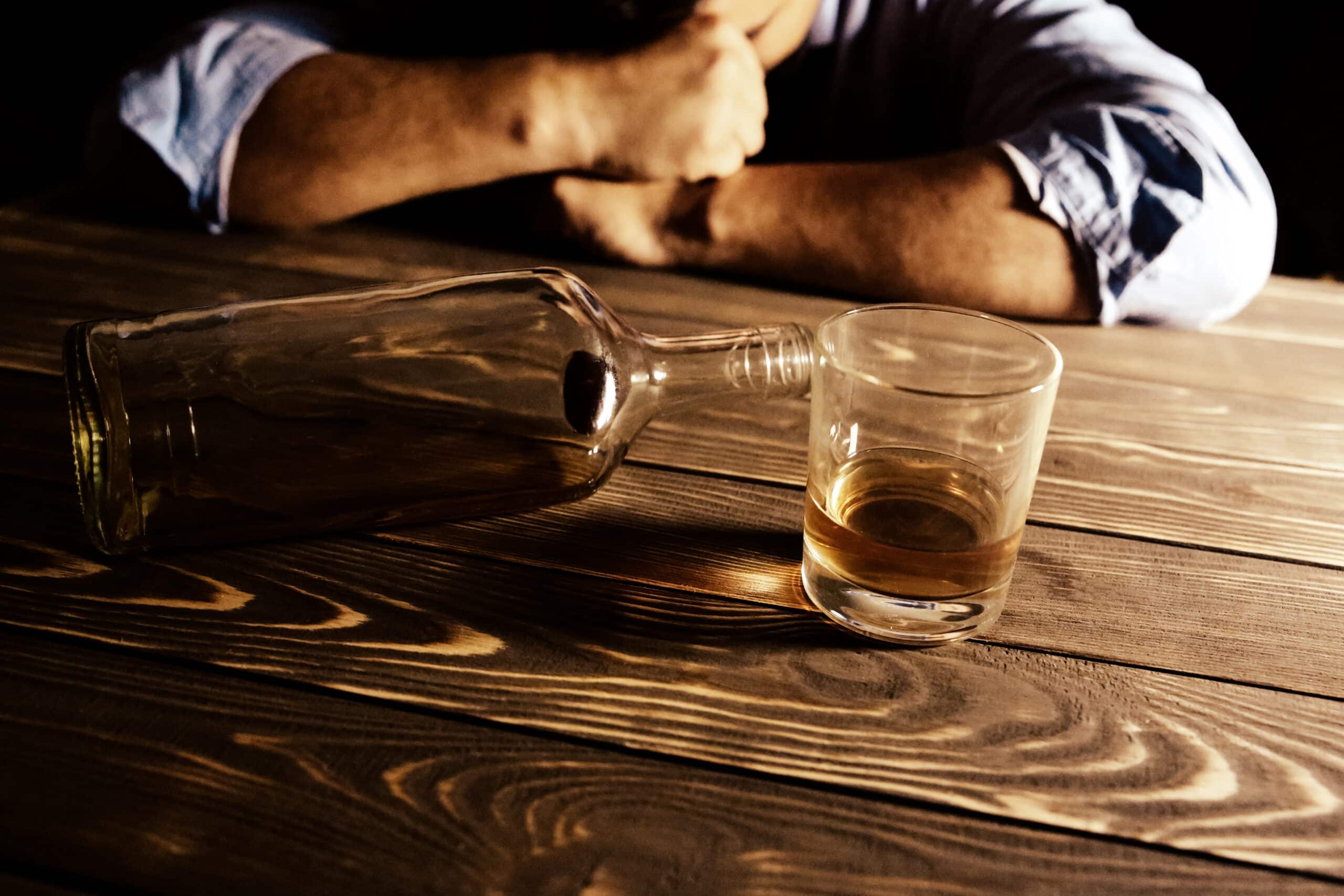 Someone sitting in front of a glass of alcohol and a tipped over bottle wondering how to cut back on drinking.