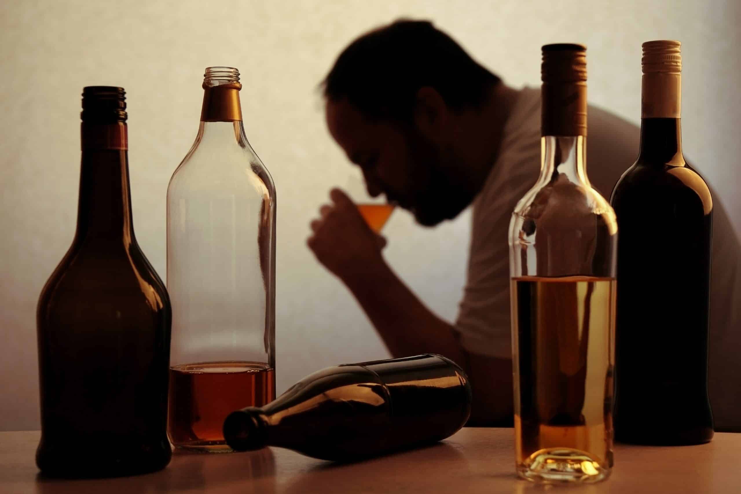 A man with alcohol tolerance sipping a glass of alcohol with several bottles in the foreground.