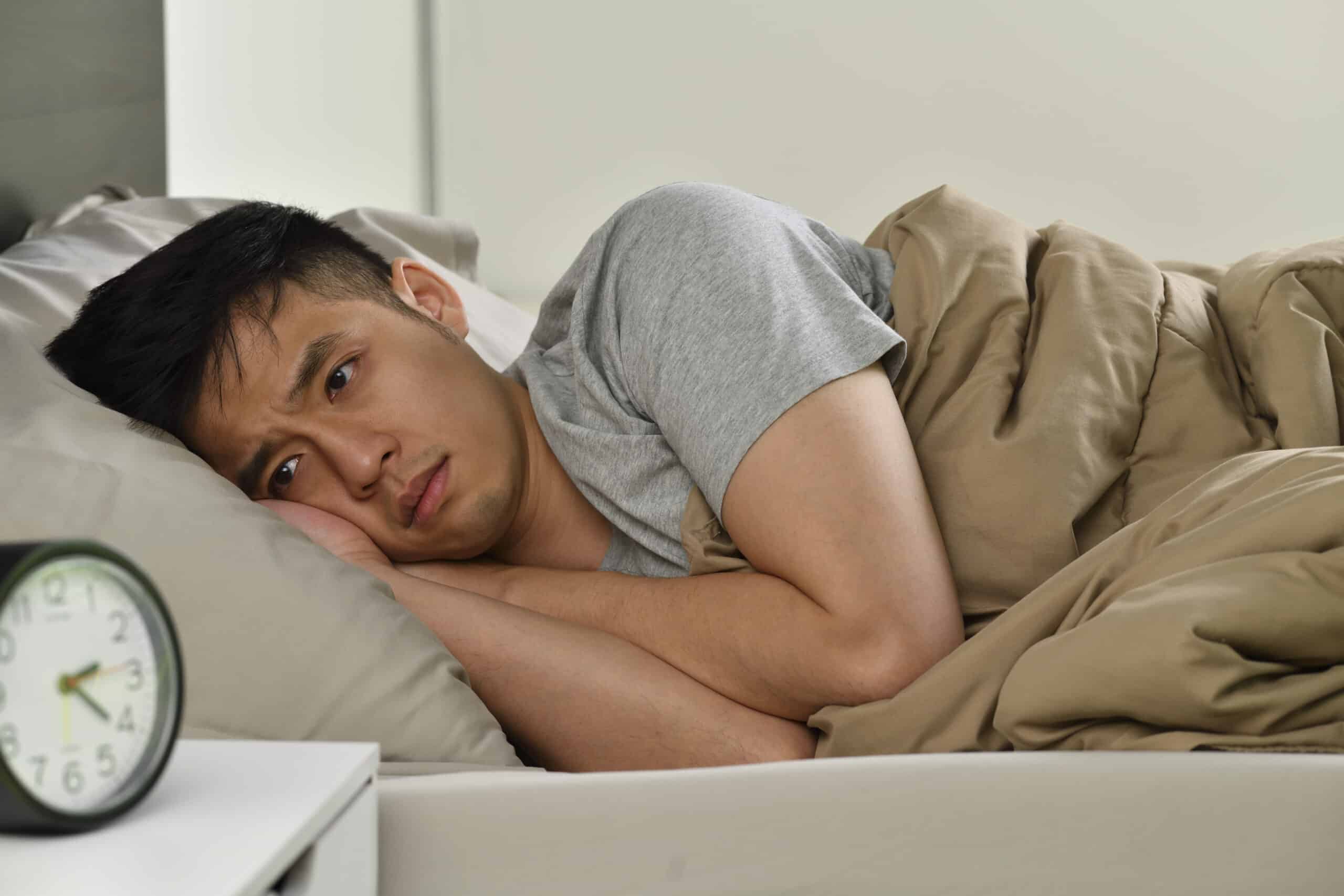 A man expericing sobriety fatigue is lying in bed and staring at a clock.