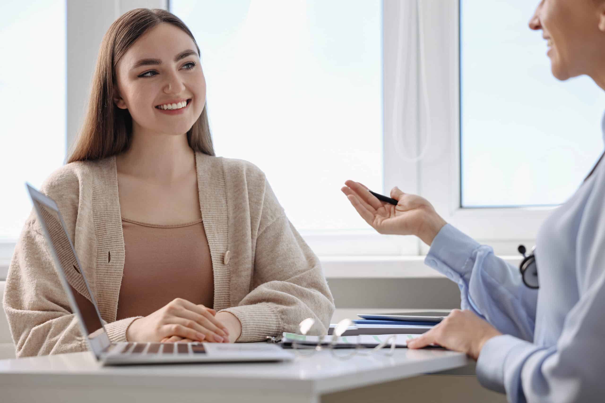 A woman sitting at a desk with a doctor and smiling while asking the question does medicaid cover suboxone.