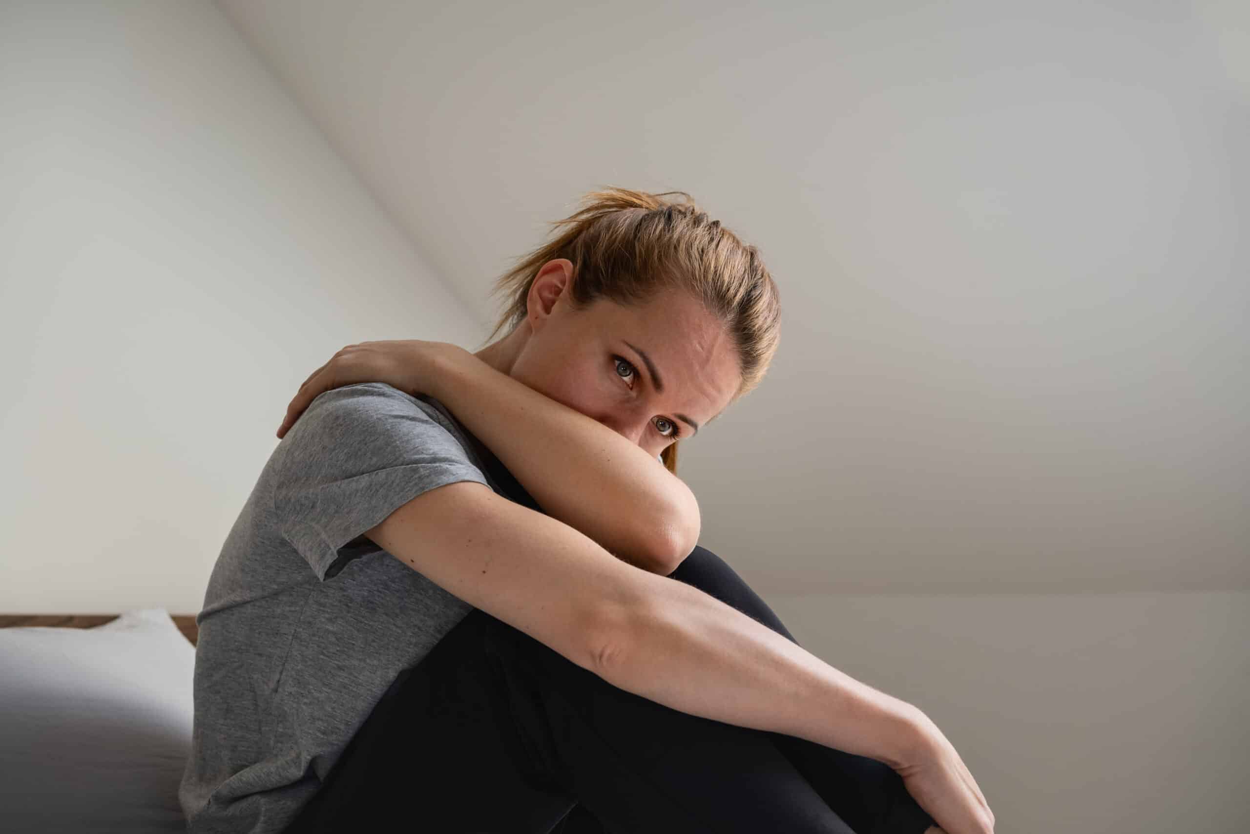 A woman going through methadone withdrawal symptoms looking sad with her head in her arms.