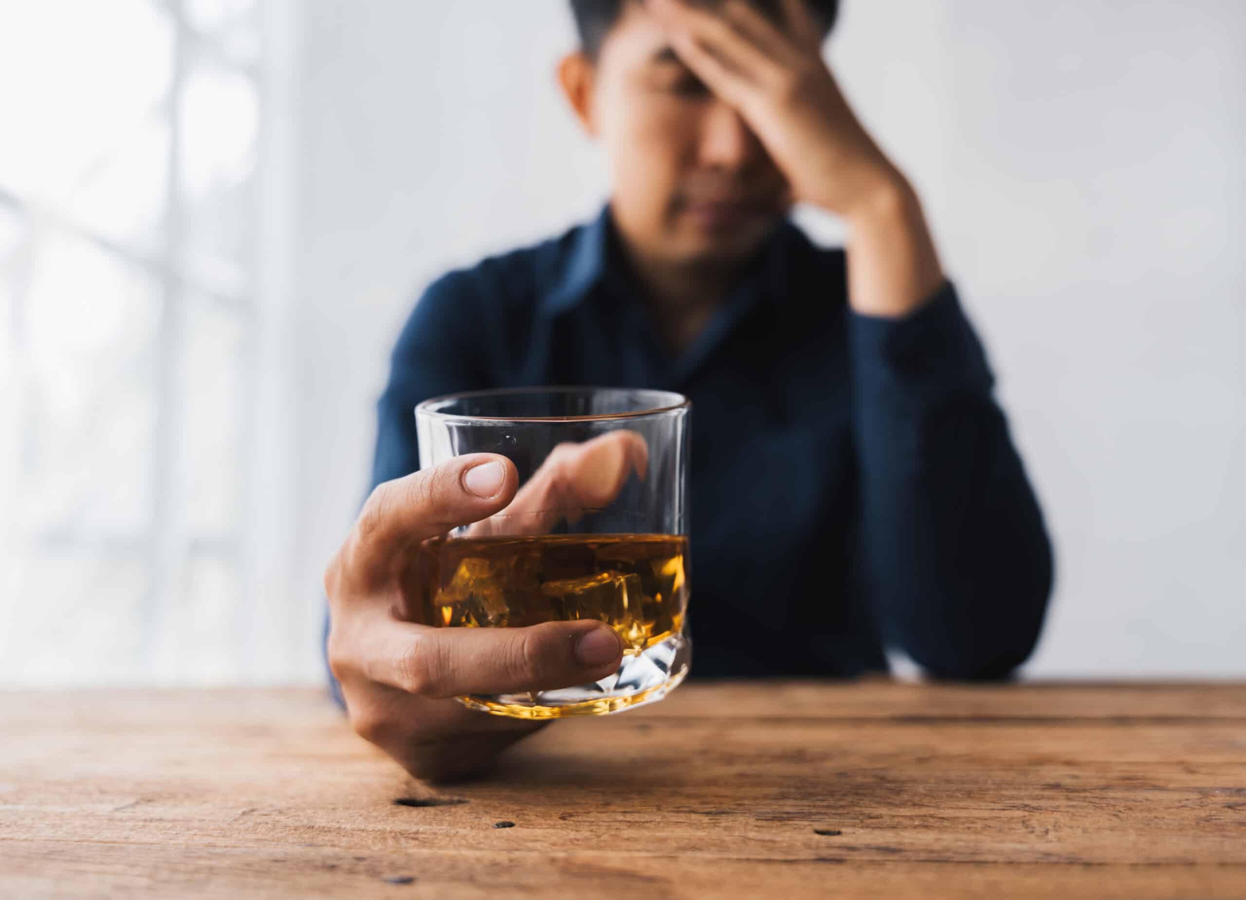 A man looking worried while holding a glass of alcohol and wondering how to stop alcohol cravings.