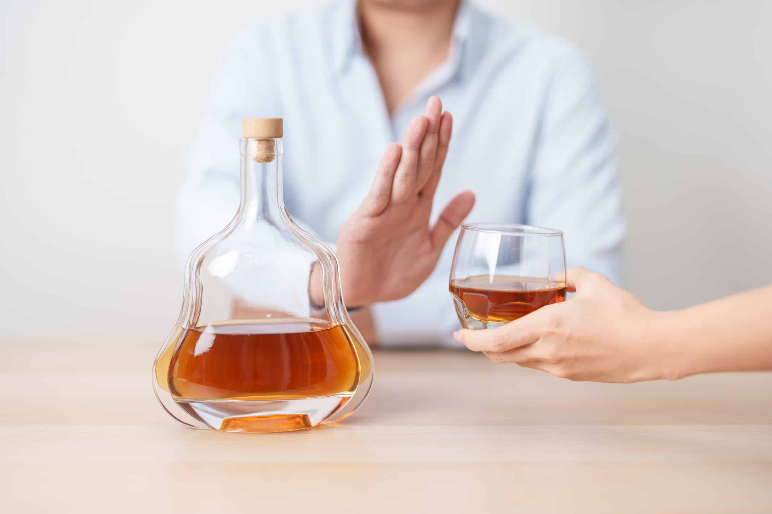 A person who is sober curious holding up their hand to refuse a glass of alcohol.