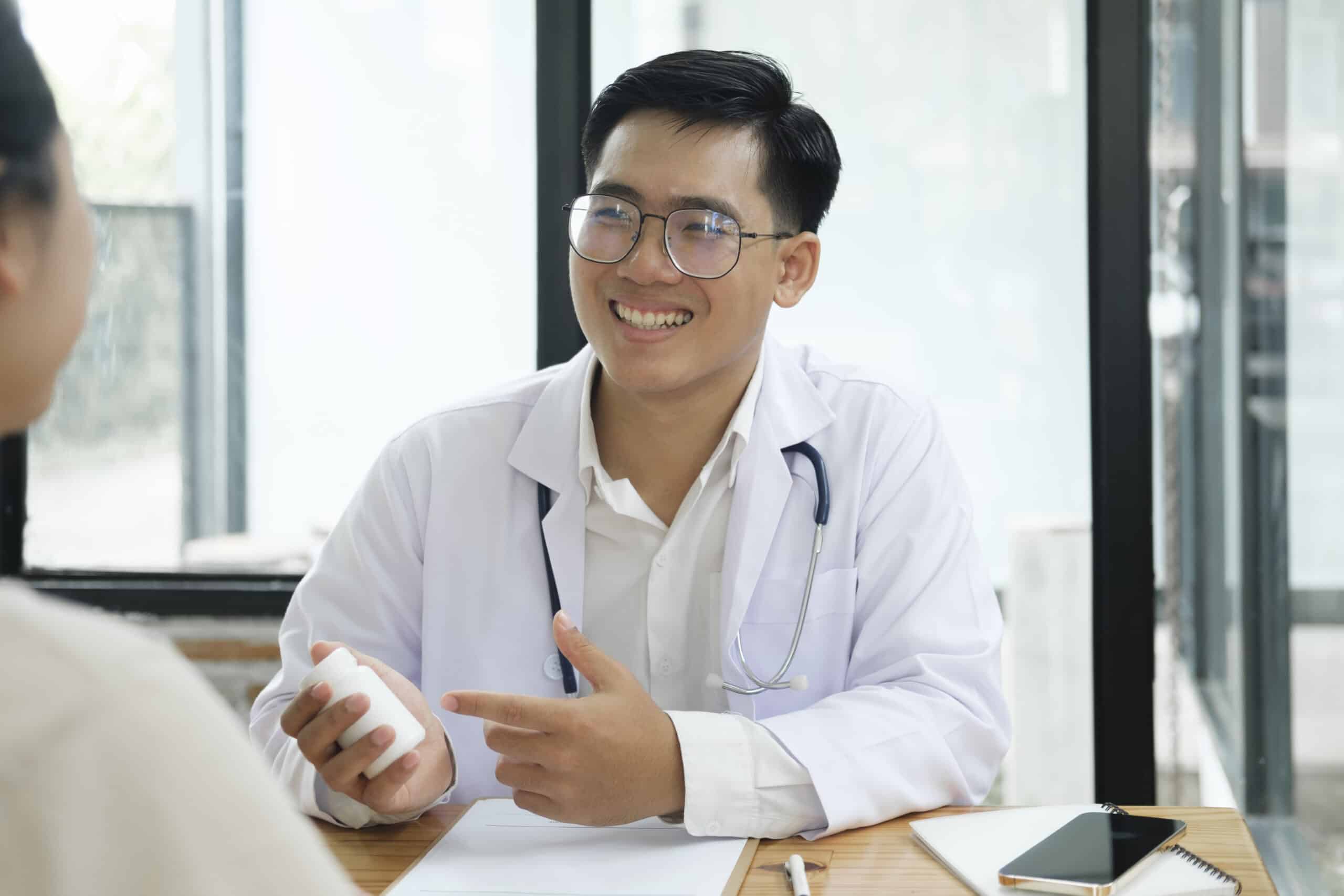 A doctor smiling at a patient while holding a pill bottle and comparing naltrexone vs suboxone.