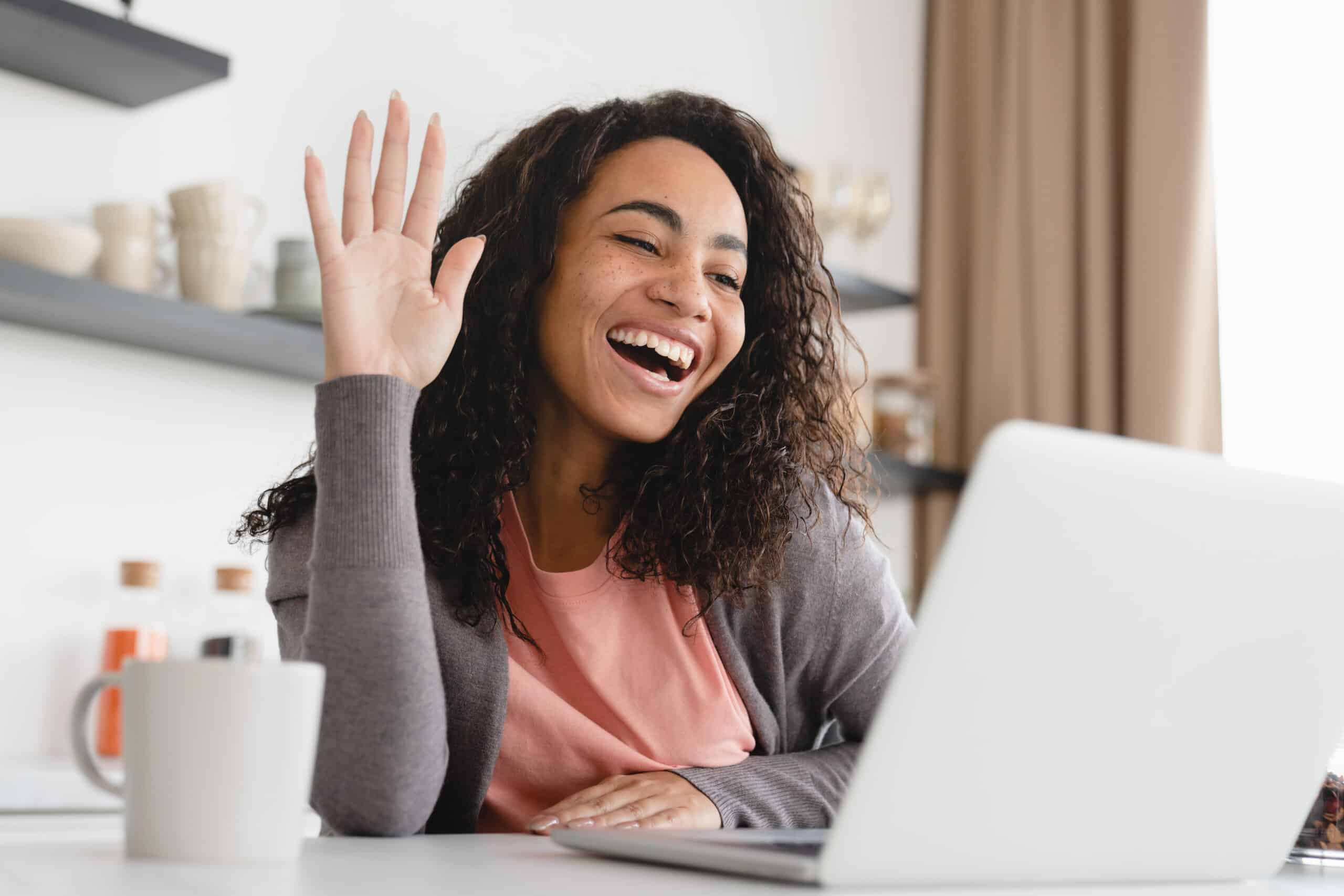 A woman waving at her laptop while on a video call for the topic telehealth for suboxone.