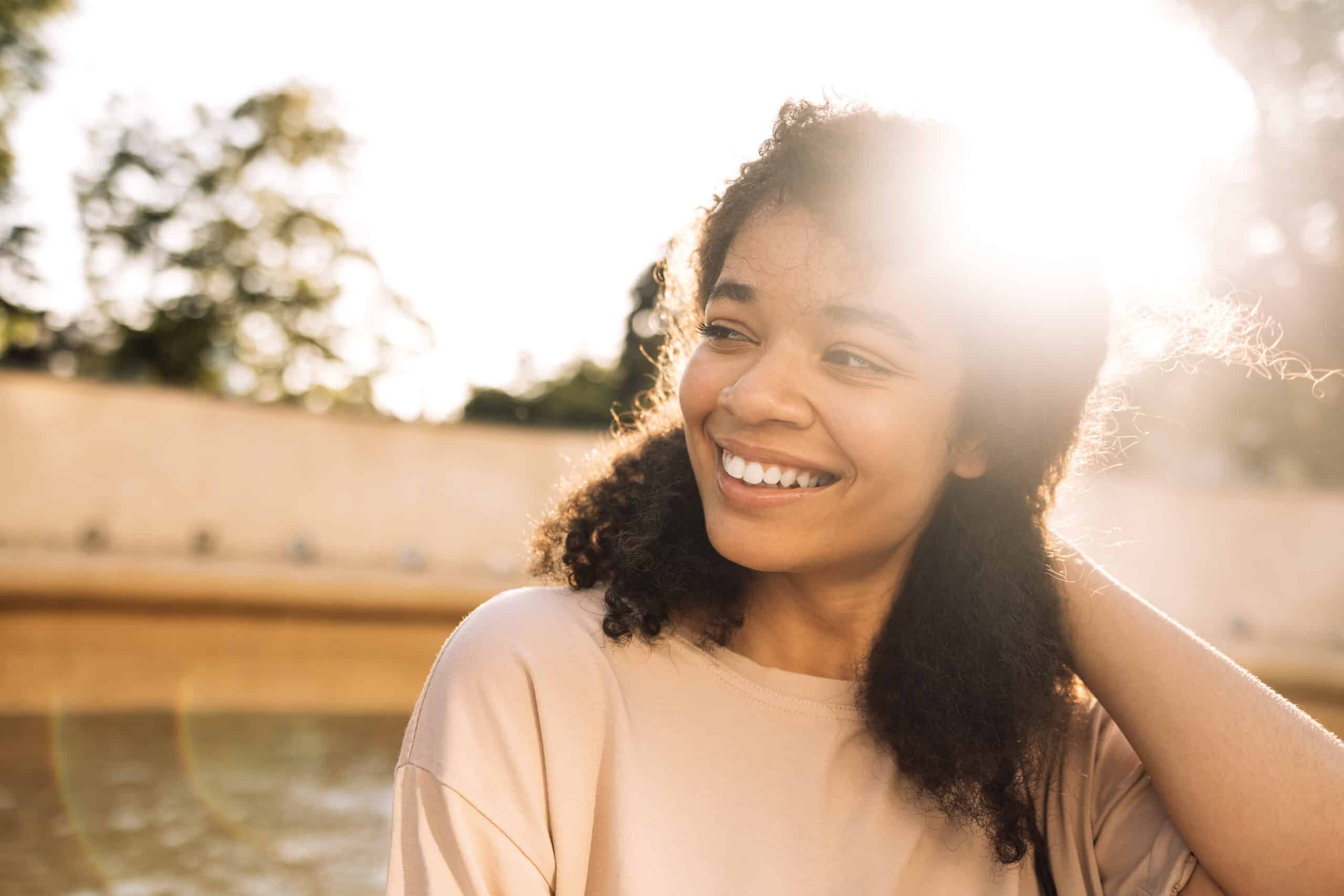 A woman smiling in a ray of sunshine for the topic the benefits of not drinking alcohol.
